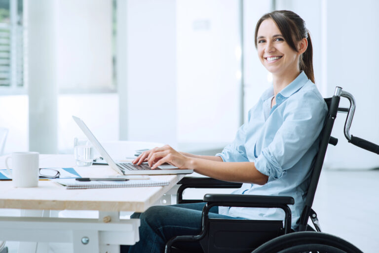 A confident happy business woman in a wheelchair working at her office desk