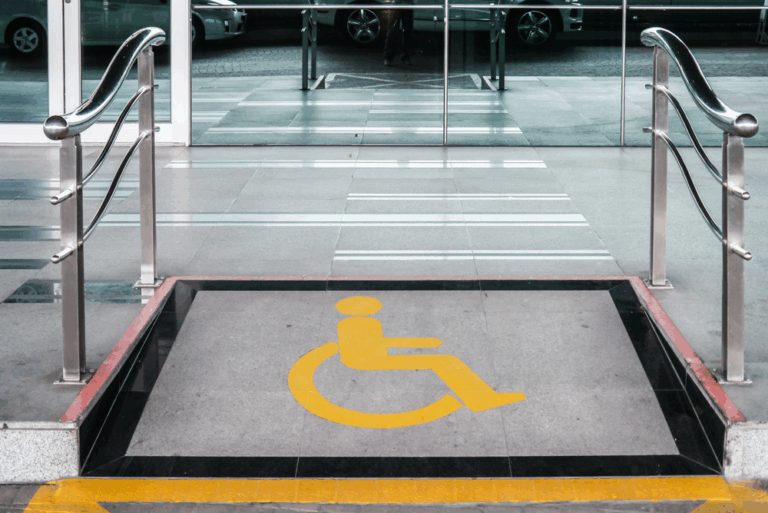 Wheelchair-accessible ramp with metal railings and a yellow accessibility symbol. The tone is inclusive, emphasizing accessibility.